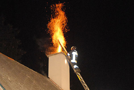 Feuer spritzt aus Kamin, Feuerwehrmann auf einer Leiter.