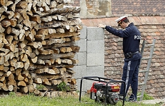 Polizist lehnt an Mauer in der Nähe des Fundorts von Julia Kührer, davor ein Holzhaufen.