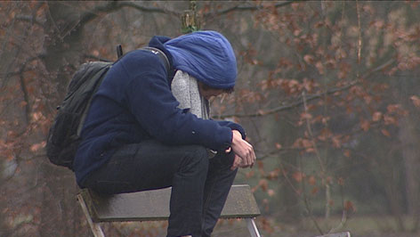 Jugendlicher anonymisiert sitzt auf einer Parkbank - Sujet