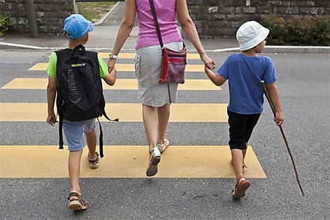 Frau geht mit zwei Kindern über Zebrastreifen