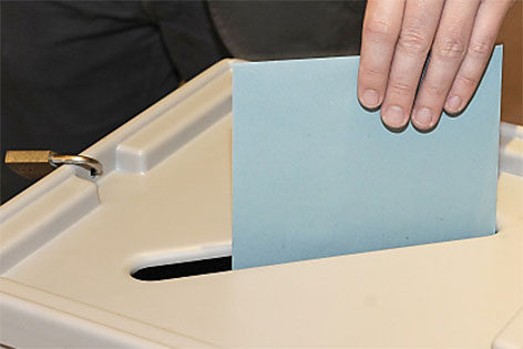 Mann wirft Kuvert in eine Wahlurne