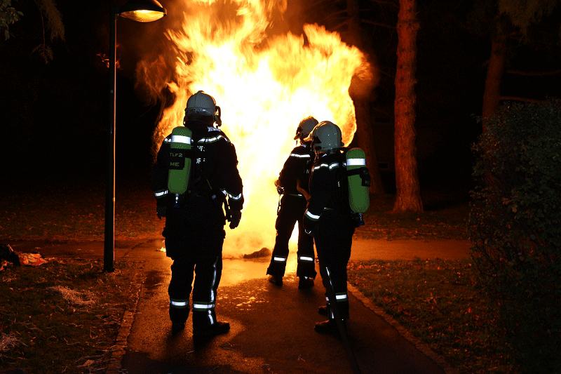 Feuerwehrleute vor brennendem Müllbehälter